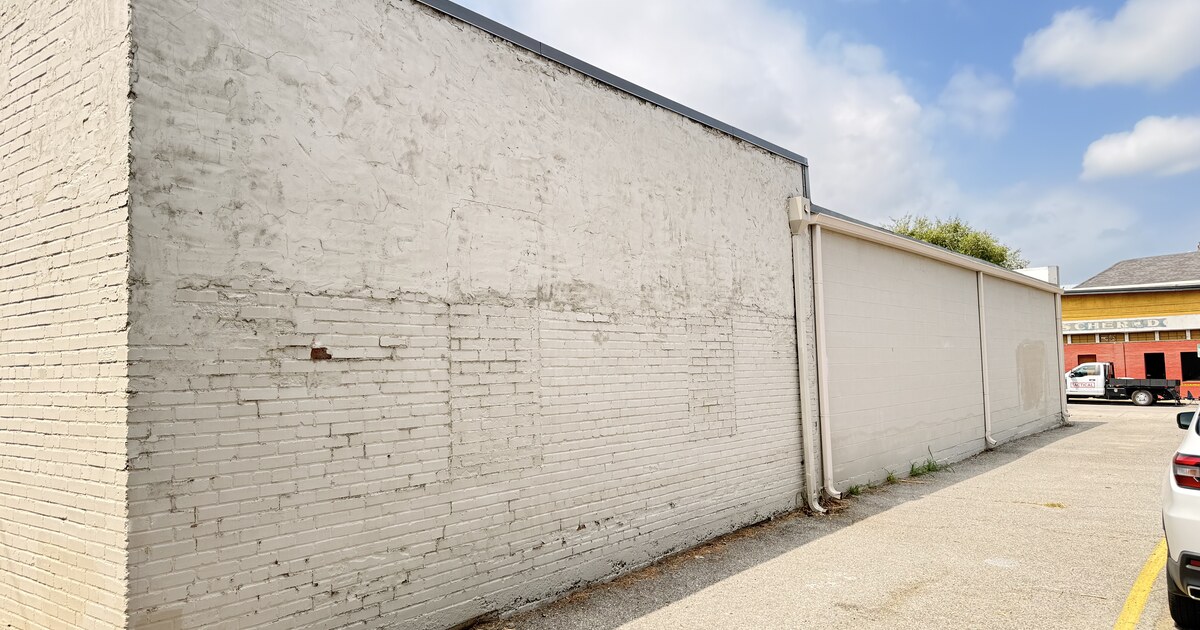 A tall painted brick wall along a parking lot at 226 E. Virginia Street, the proposed mural site, under a partly cloudy sky.